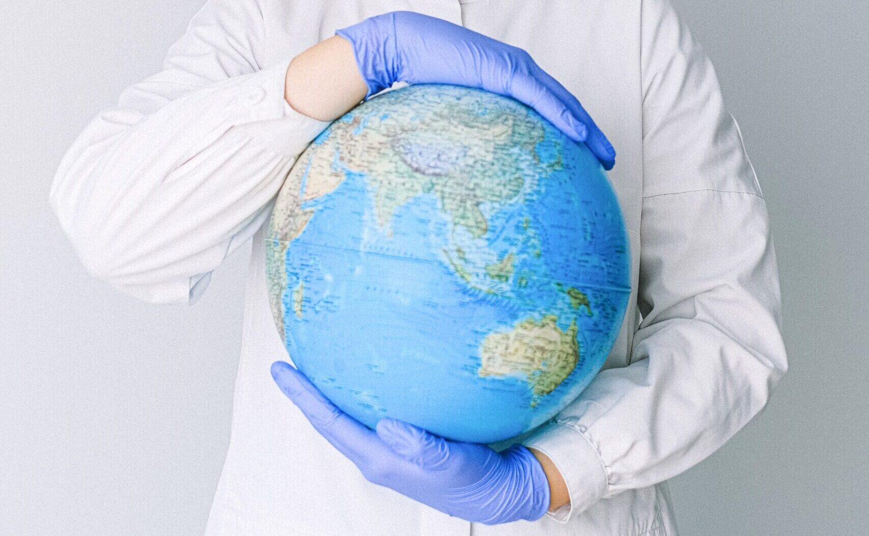 Person wearing a clinical white coat and gloves holding a globe