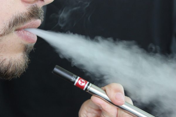 Person holding an e-cigarette and blowing smoke