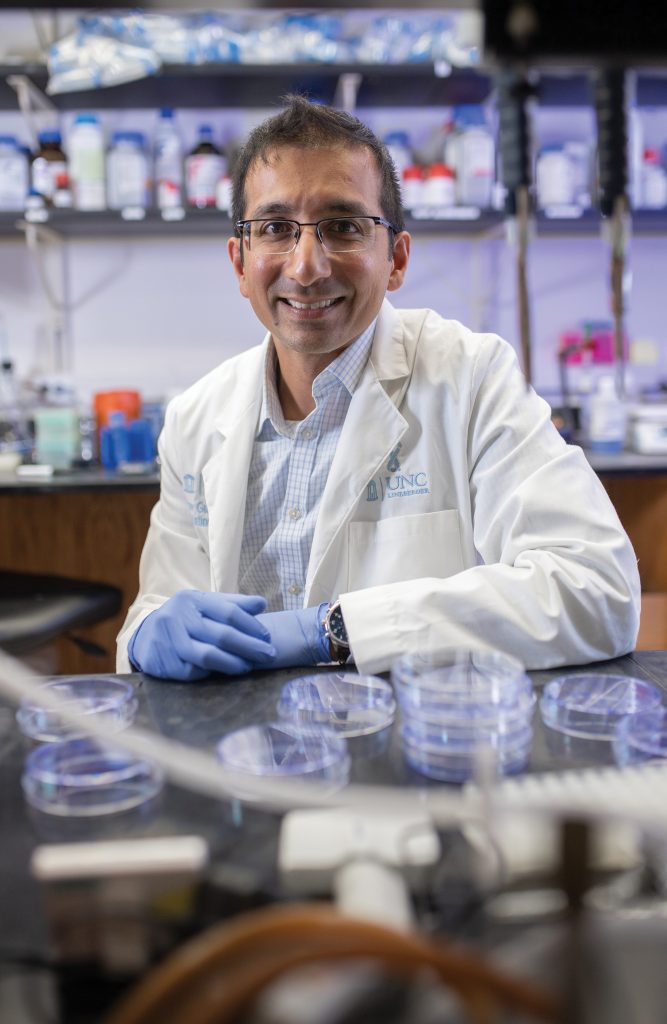 Gaorav Gupta wearing a white coat, sitting at a lab bench.