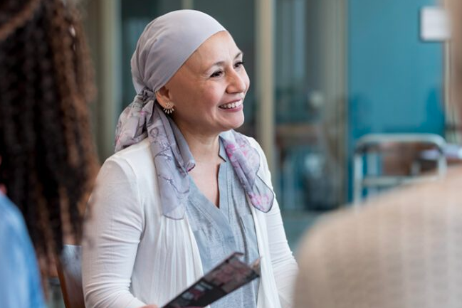 A cancer patient meets with her care team. She is smiling and wearing a headscarf.