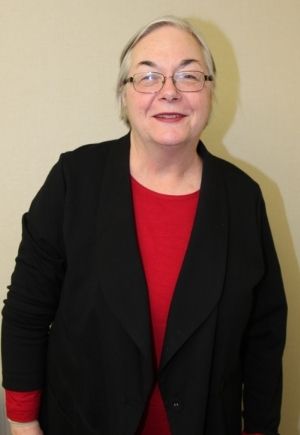 A smiling woman with short gray hair wearing glasses, a red shirt and black cardigan.