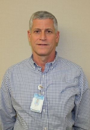 A man with short gray hair wearing a blue checkered buttoned shirt.