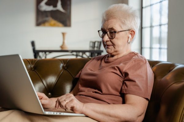 An older woman wearing glasses uses a laptop and headphones for a telehealth visit.