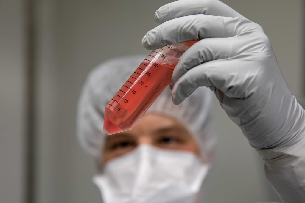 A person wearing medical protective equipment holds a vial of red liquid.