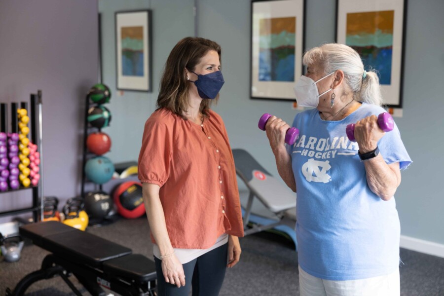 A patient lifts hand weights while working with a trainer.