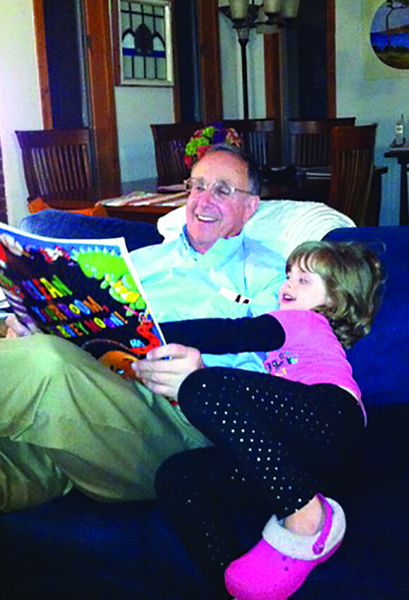 Man sitting on a sofa reading a children's book with a young girl.