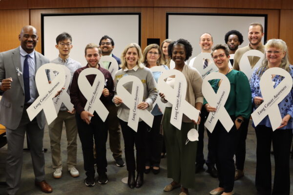 A group poses with large white ribbons in recognition of Lung Cancer Awareness Month