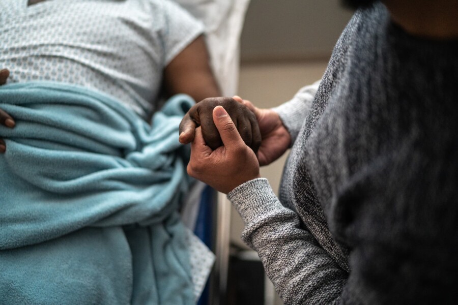 Patient in a hospital bed holds their caregiver's hand