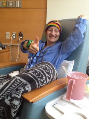 Janine Jones smiles and gives a thumbs up while sitting in a chair in a hospital room