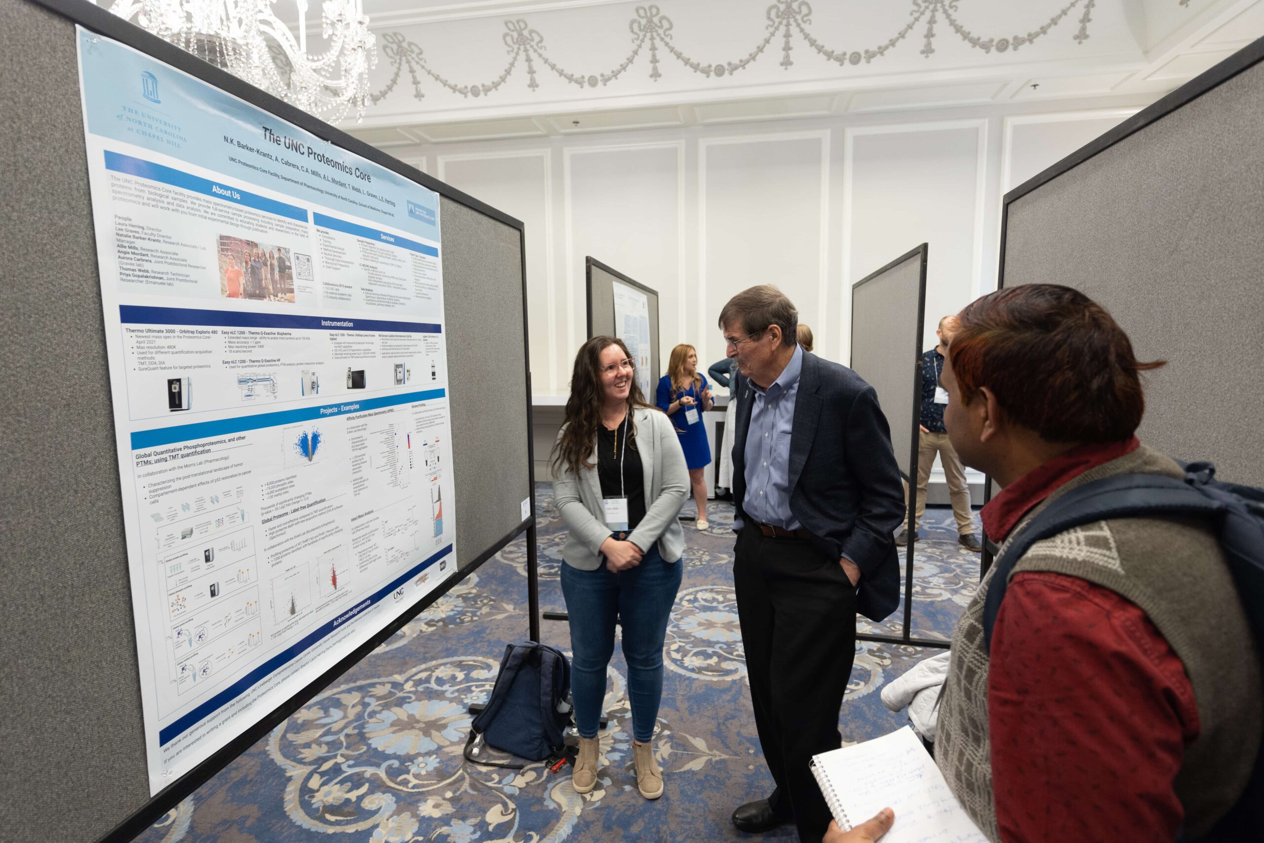 Three people gather around a scientific poster and discuss the UNC Proteomics Core facility