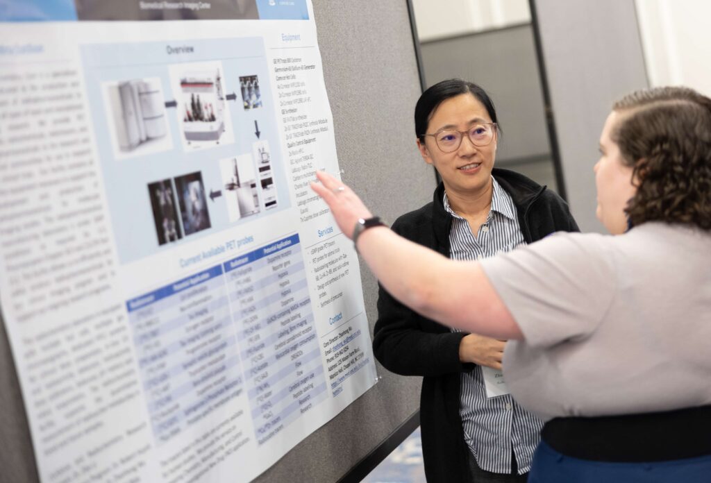 Two people gather around a scientific poster and discuss a shared resources facility