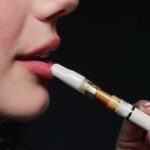 A teen girl holds an e-cigarette to her mouth.