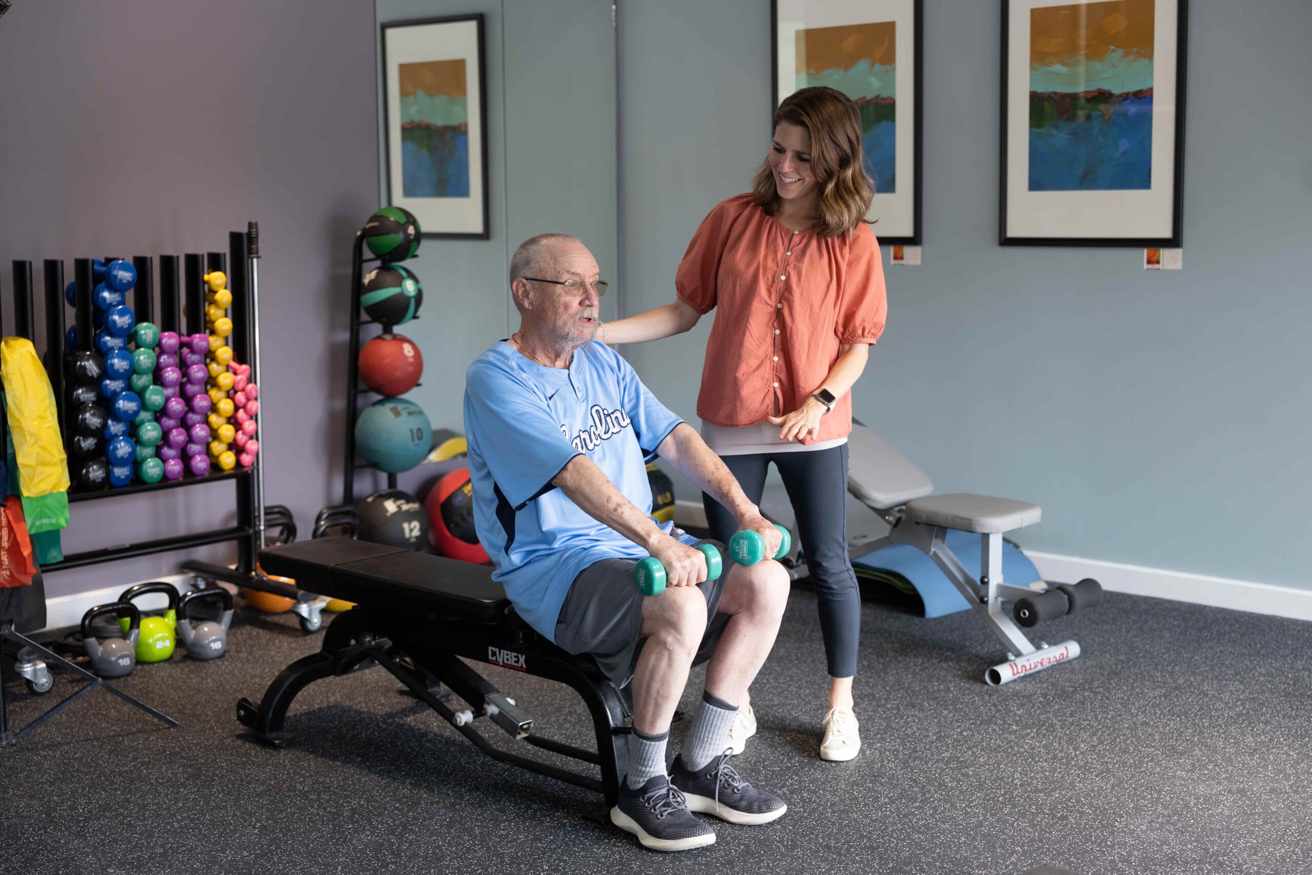 A patient lifts hand weights with a Get Real & Heel trainer.