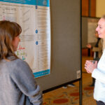 Two people talk next to a research poster at the 13th annual UNC-Duke Viral Oncology and AIDS Malignancy Symposium.