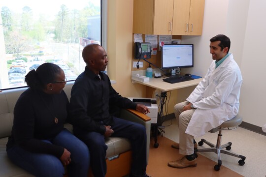 Oncologist Sid Sheth meets with a patient and their caregiver in a clinic room.